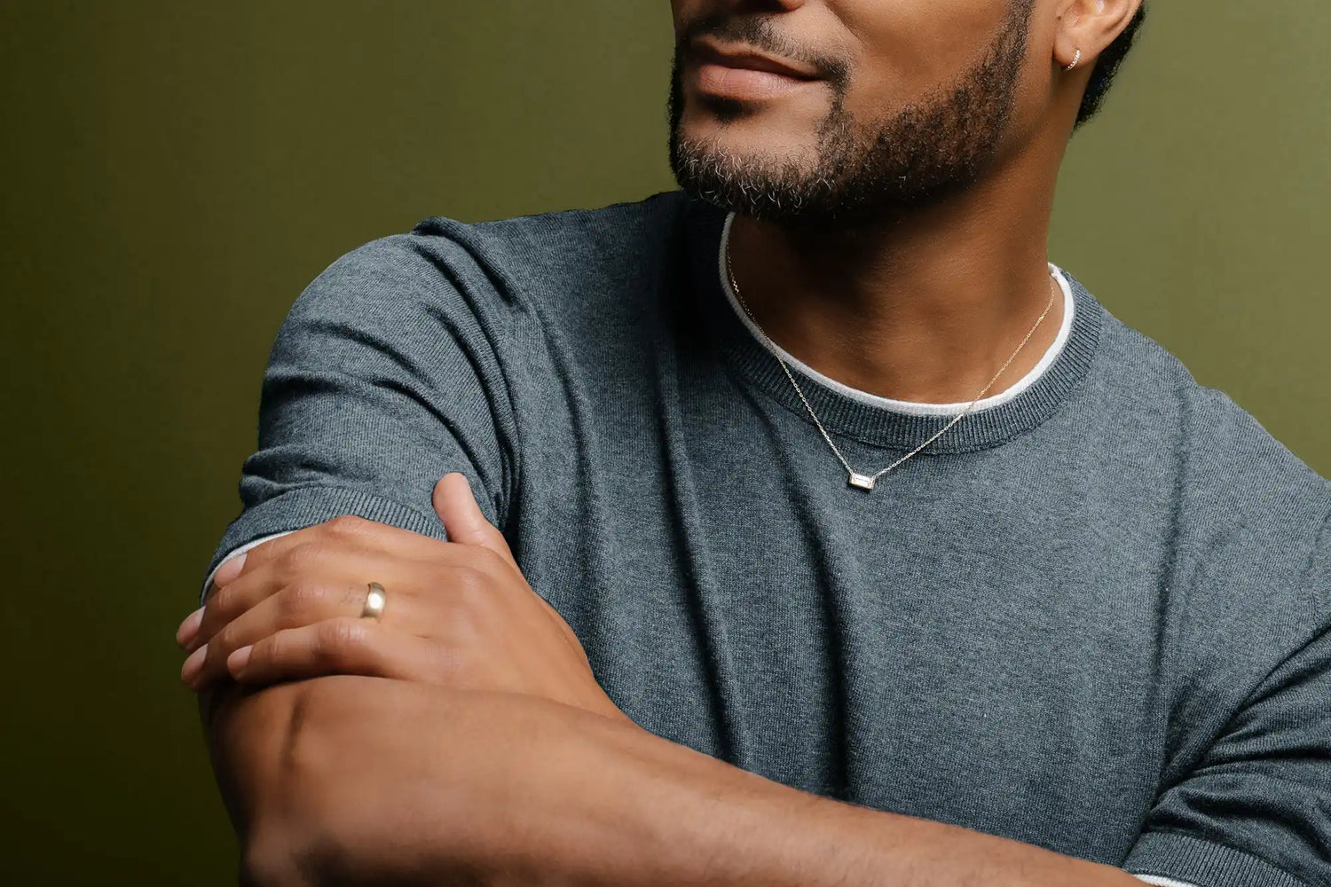 Man with a beard wearing a gray shirt and silver necklace, arms crossed